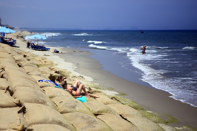 Hai nữ du khách nước ngoài nằm phơi nắng ngay trên những bao bố nhồi cát chặn sóng trước đây. Nhiều bao bố đã phủ rêu xanh. 