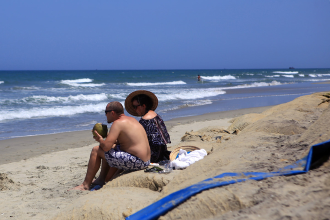 Du khách dạo chơi, ngồi uống nước giải khát trên bãi biển, khi xung quanh vẫn còn ngổn ngang những bao bố. 