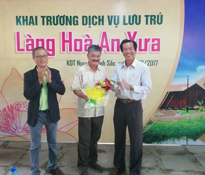 Ông Nguyễn Ngọc Thương, Giám đốc Sở VHTTDL (bìa phải) tăng hoa cho đơn vị tư vấn khai thác dịch vụ các căn nhà gỗ thuộc làng Hòa An xưa 